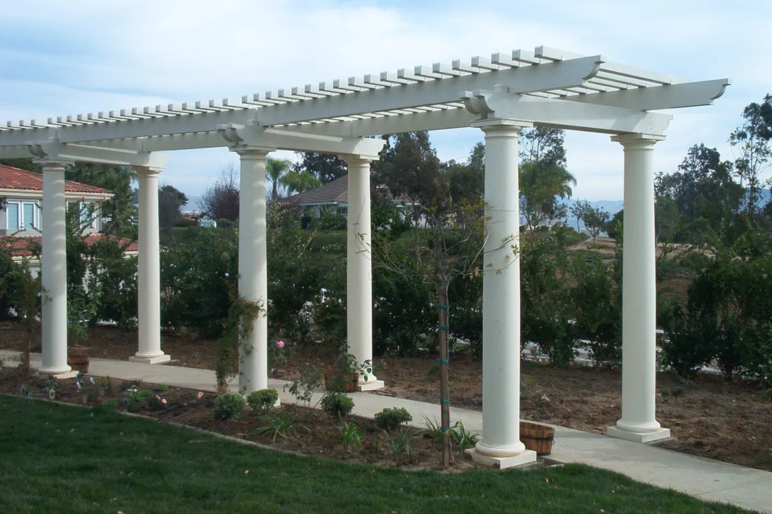 Long white pergola with round classical columns over a paved garden walkway in a backyard garden