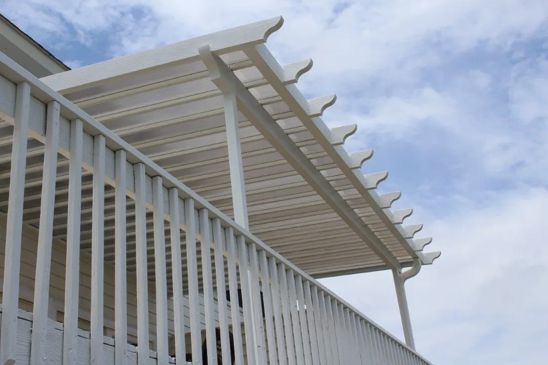 White pergola with curved rafter ends above a matching vertical railing under a cloudy sky