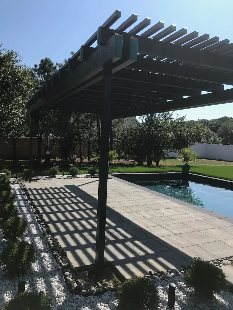 Black wood pergola shading a stone patio next to an outdoor backyard swimming pool