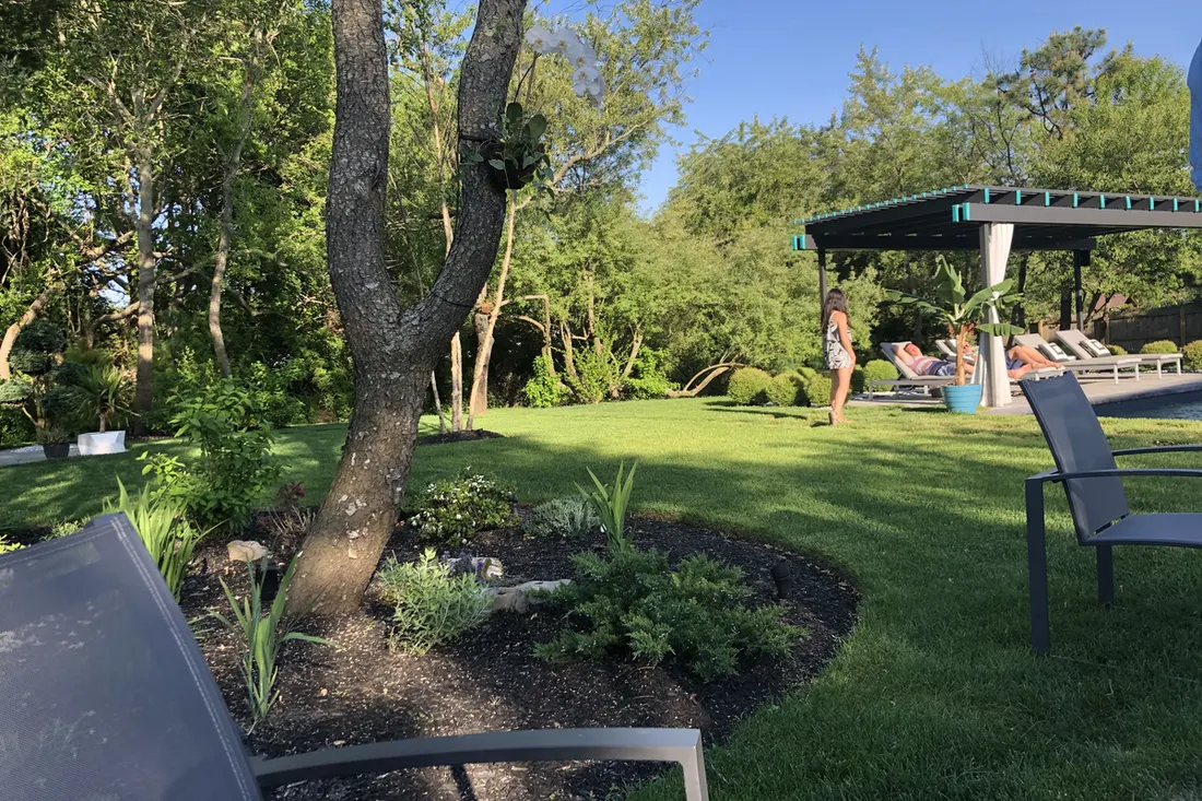 Black-roofed pergola with teal accents and lounge seating beside a landscaped lawn and garden