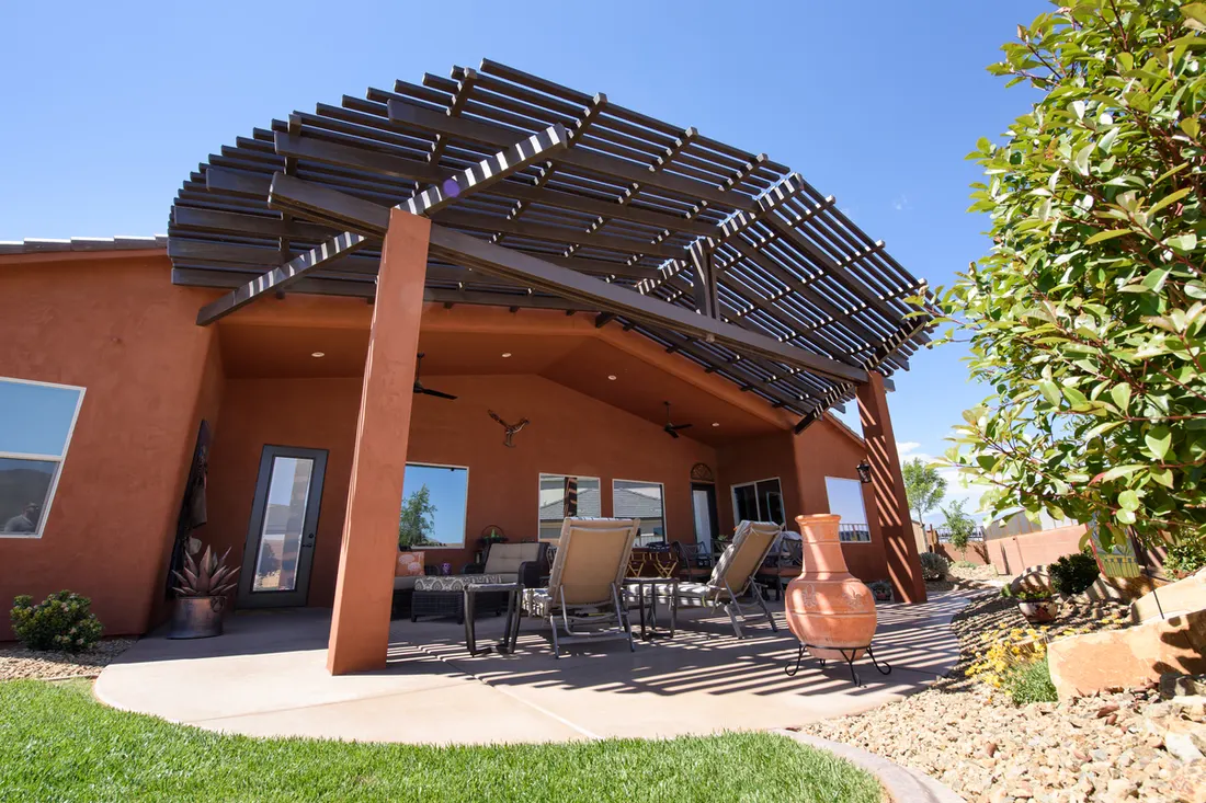 Terracotta stucco patio with dark wood pergola, outdoor seating, grill, lawn, and desert landscaping