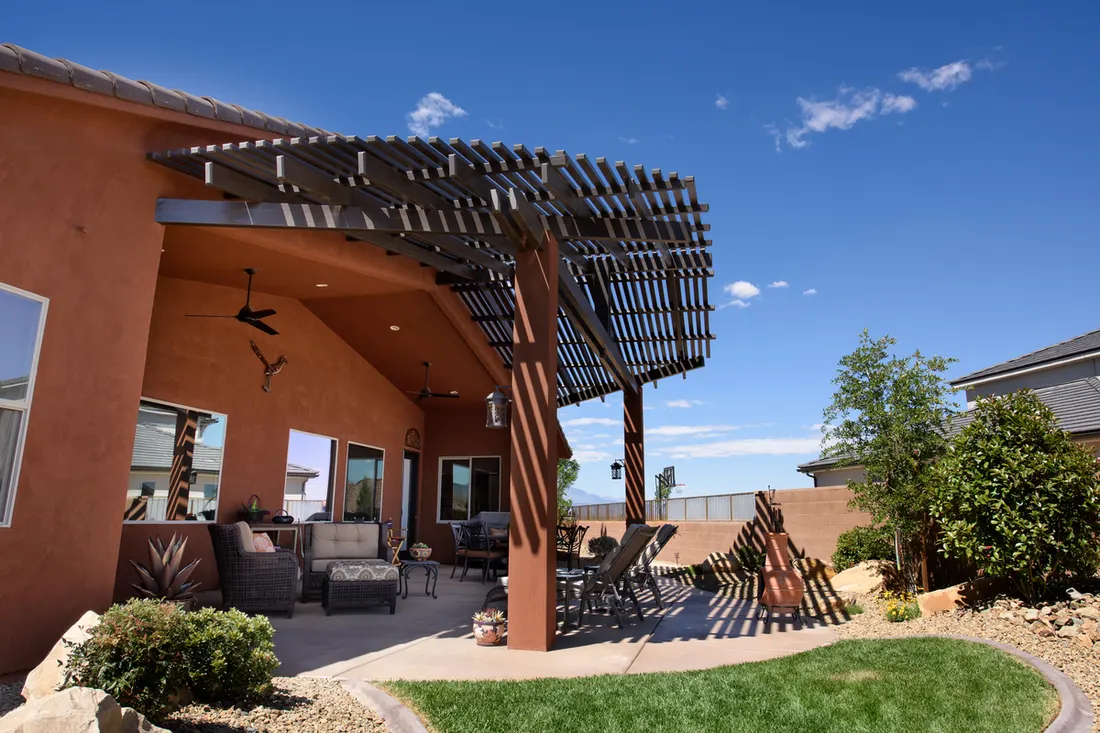 Dark wood pergola attached to terracotta stucco home, shading a paved patio and backyard