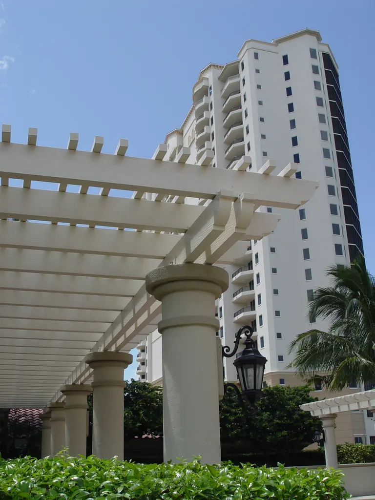 White pergola with round columns and hanging lantern outside a high-rise building