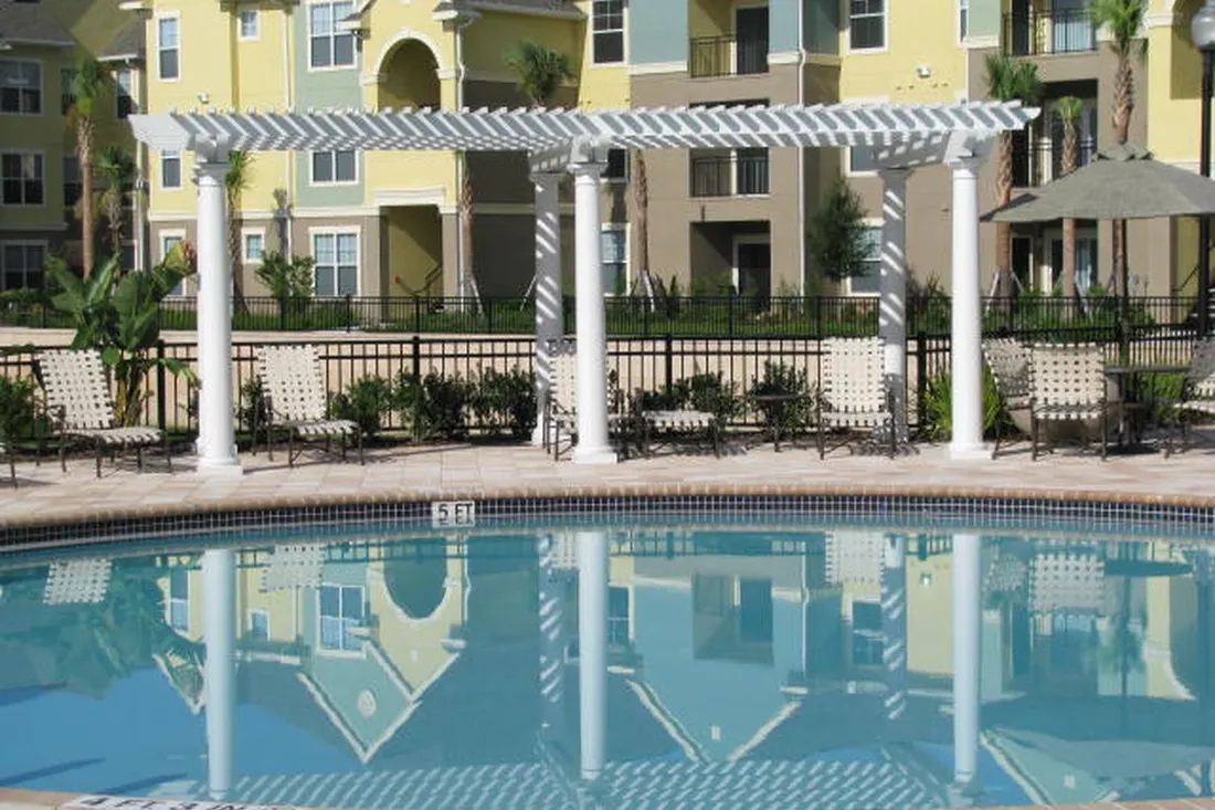 White pergola with slatted roof and columns beside a swimming pool in a landscaped courtyard