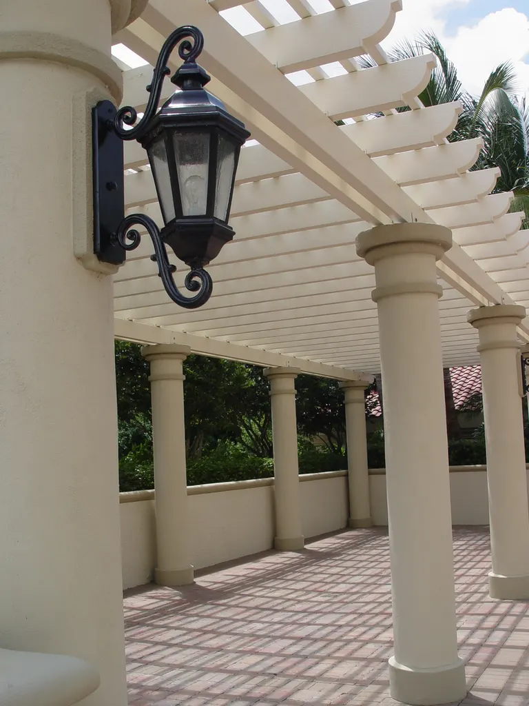 White pergola supported by round stucco pillars over a paved patio with an attached black lantern