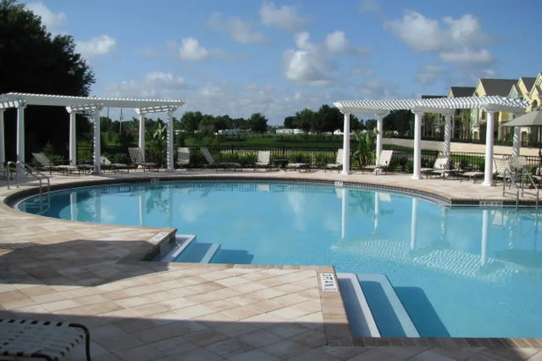 White vinyl pergolas beside a swimming pool with a stone paver patio and lounge chairs