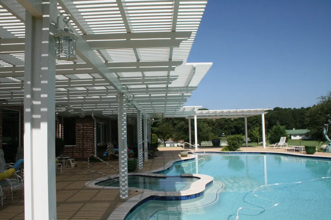 White pergola shading a poolside patio with hot tub against a blue sky background