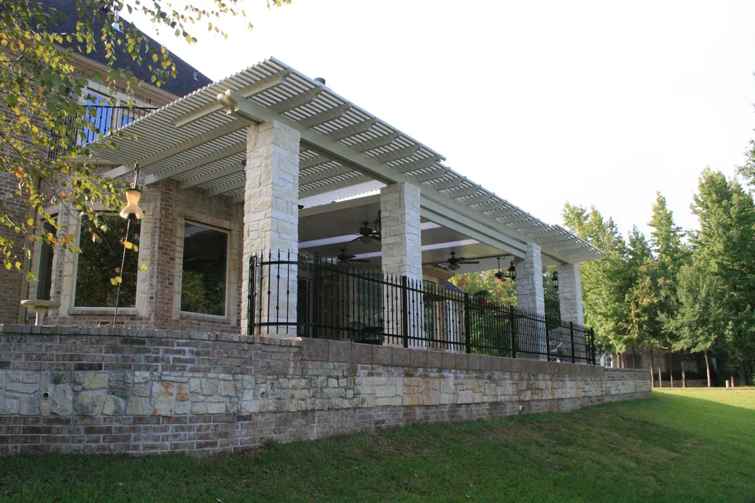 White stone pergola with slatted roof, brick pillars, black railings, and a grassy yard