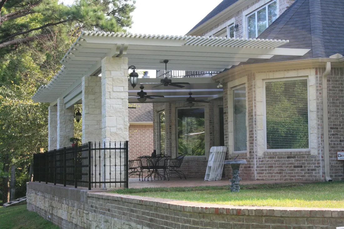 White patio pergola with ceiling fans attached to brick house supported by stone pillars