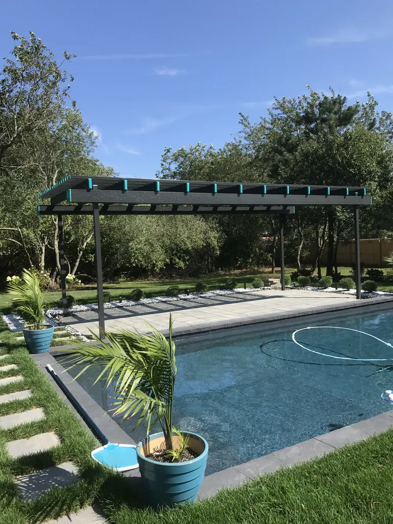 Black metal pergola with slatted roof beside a swimming pool, surrounded by trees and potted palms