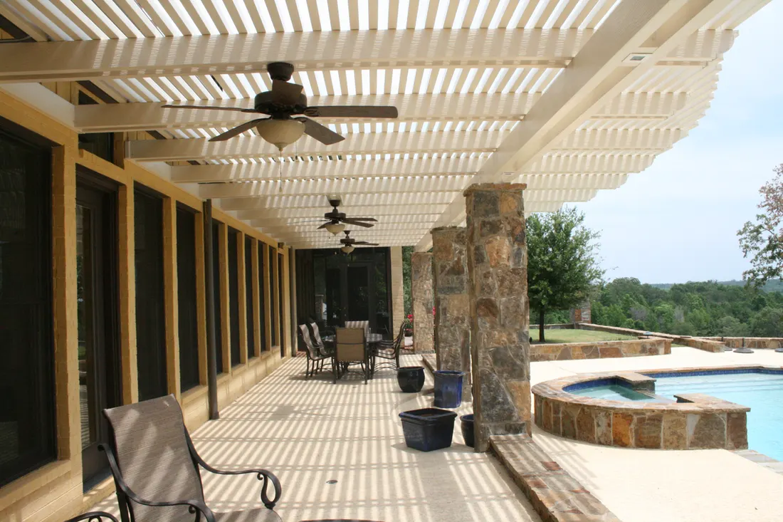 White slatted pergola covering a stone-columned patio beside a pool and countryside view