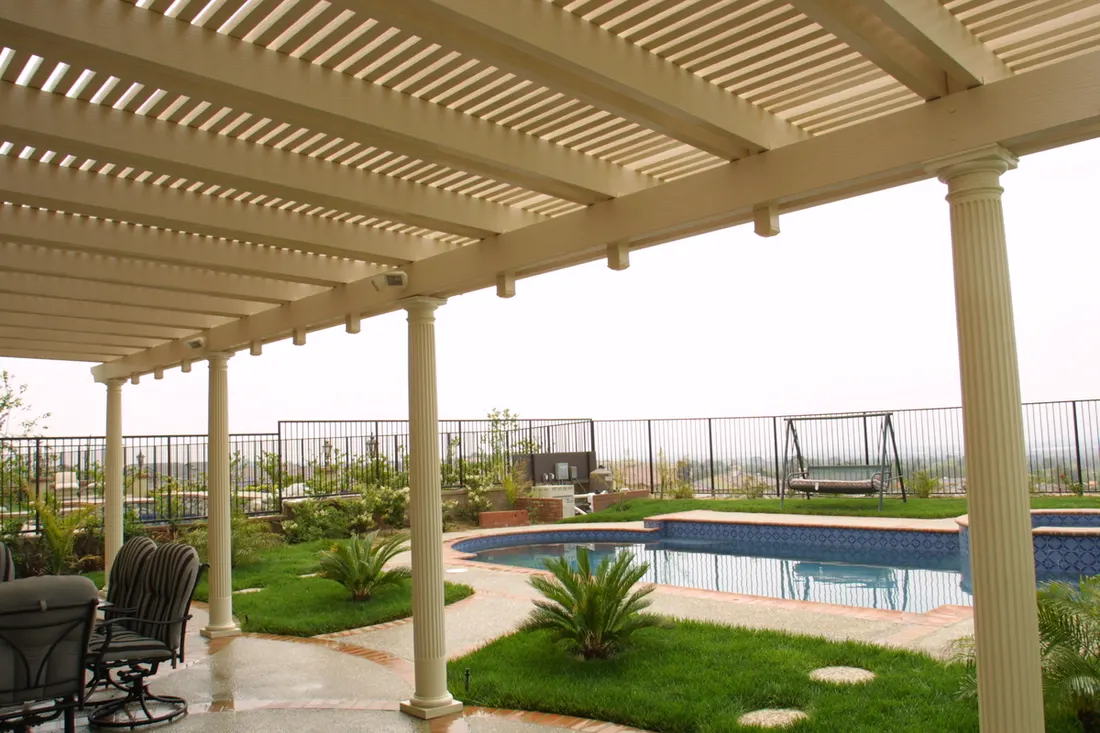 Cream pergola with slatted roof and columns overlooking a landscaped pool area and fenced yard