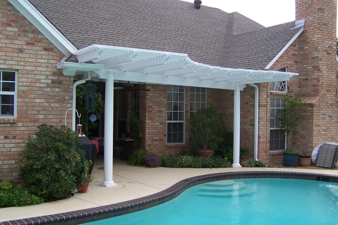 White pergola with columns beside a curved swimming pool and brick house