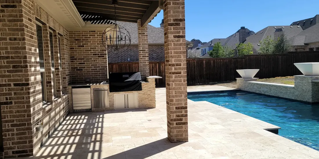 Brick-covered patio with outdoor kitchen beside a blue swimming pool and raised spa