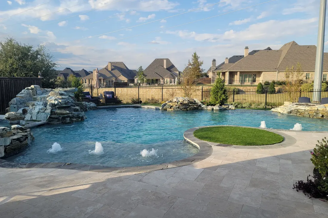 Freeform backyard pool with rock waterfall, water jets, curved stone patio, and grassy island