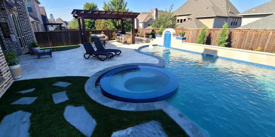 Backyard pool with attached round spa, pale stone decking, pergola, and artificial turf