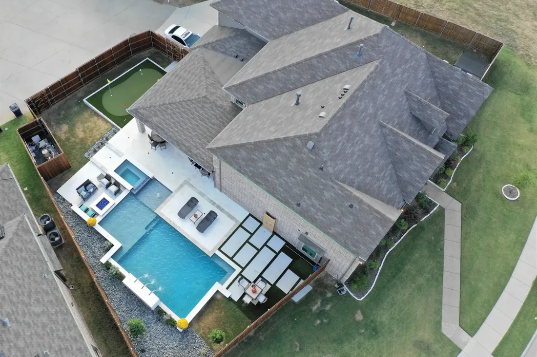 Aerial backyard with blue pool, raised spa, white decking, gray roof, and surrounding lawn