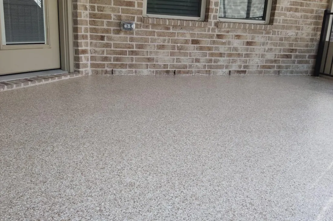 Textured light gray coated concrete patio beside a brick house with windows and a door