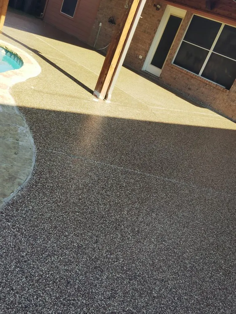 Textured dark gray pool deck coating beside a curved pool edge and brick home