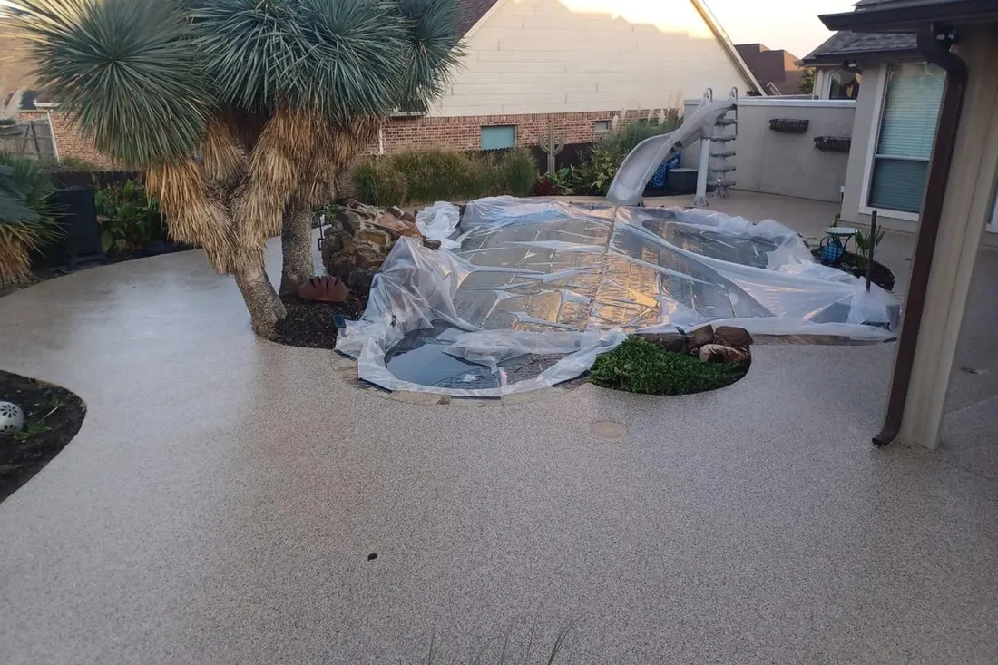 Textured light-gray pool deck surrounding a covered swimming pool and desert landscaping