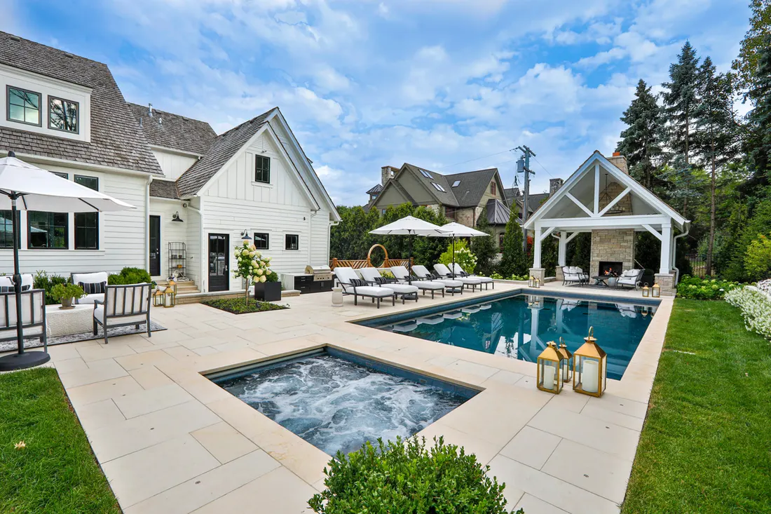 Light gray pool deck surrounds a swimming pool and raised spa beside a white pavilion