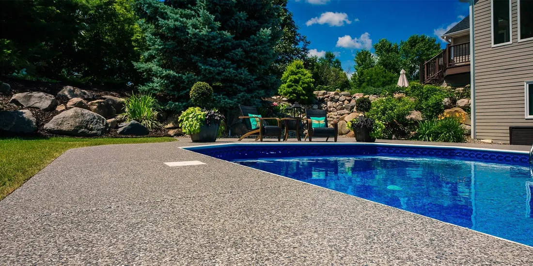 Pool deck coated in speckled gray finish beside a blue pool and rock landscaping