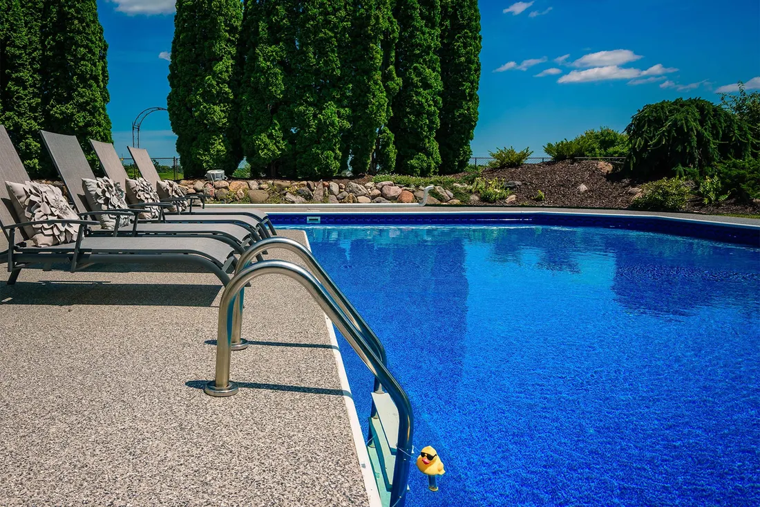Speckled pool deck coating around an in-ground pool with ladder and lounge chairs