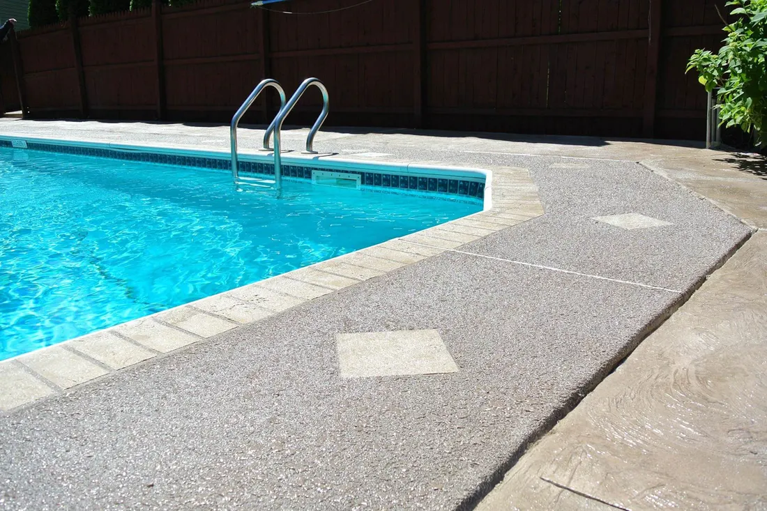 Gray textured coating on a concrete pool deck beside a pool corner and ladder