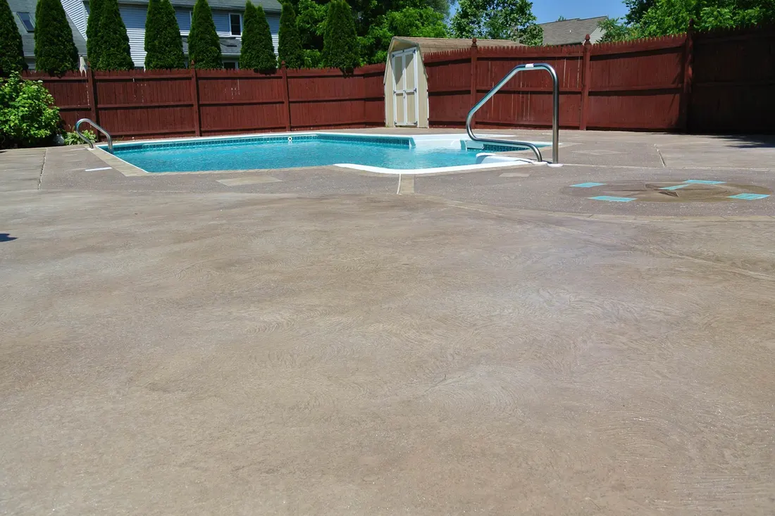 Coated concrete pool deck surrounding a small in-ground pool behind a wood fence