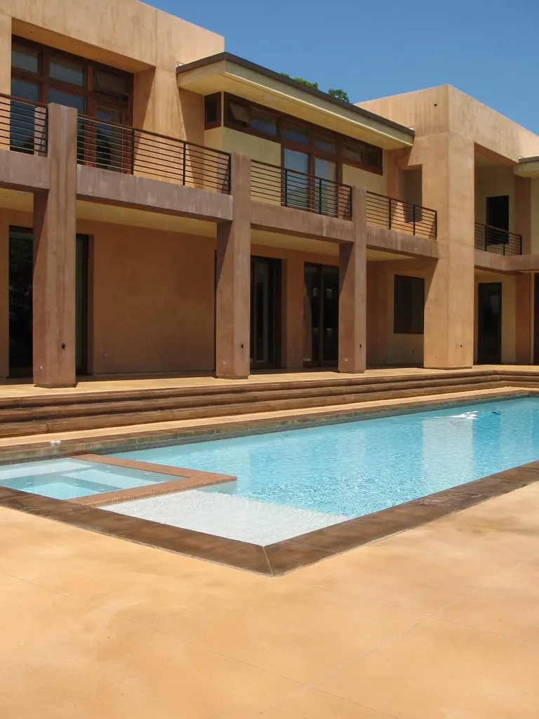 Tan coated pool deck and steps beside a pool at a two-story stucco home