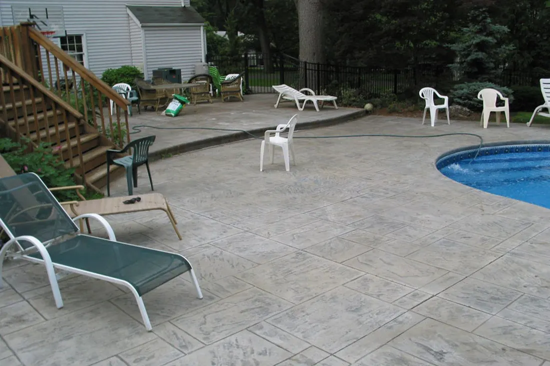 Stamped and stained concrete pool deck with lounge chairs beside a curved pool
