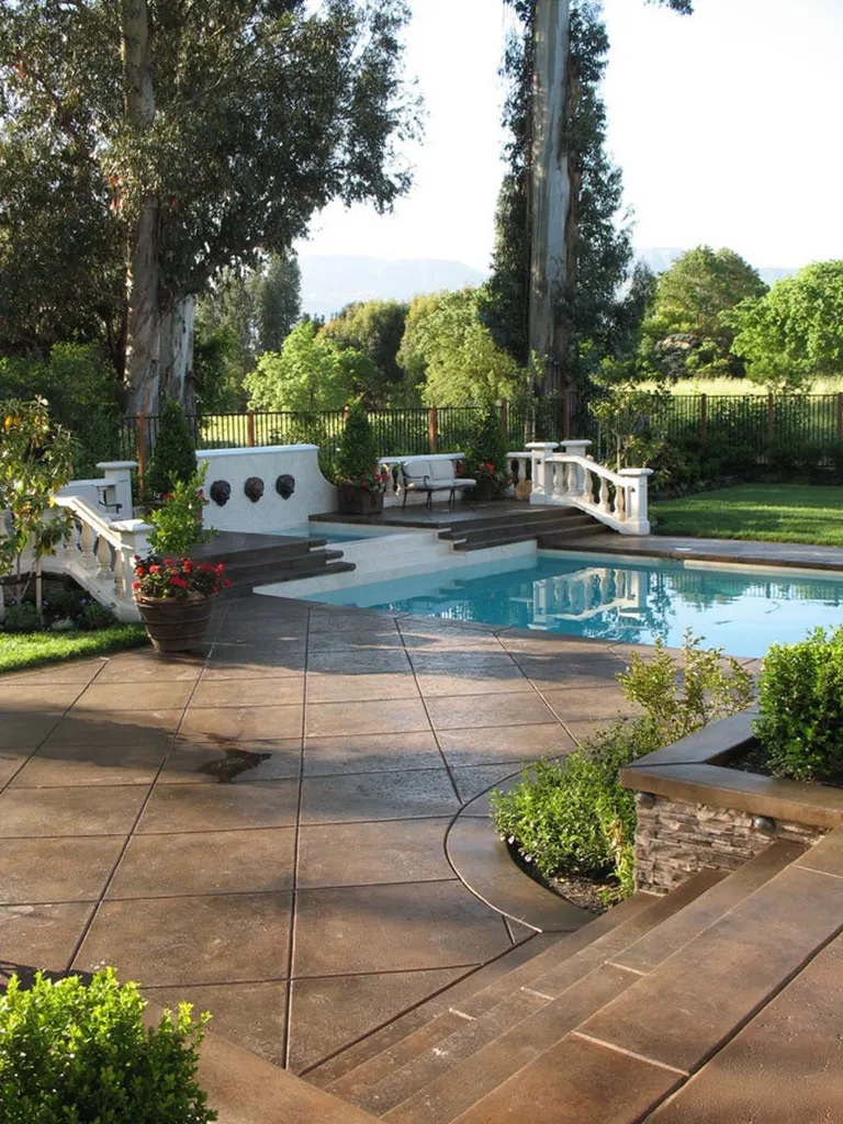 Brown stained concrete deck winding around a pool and garden landscaping