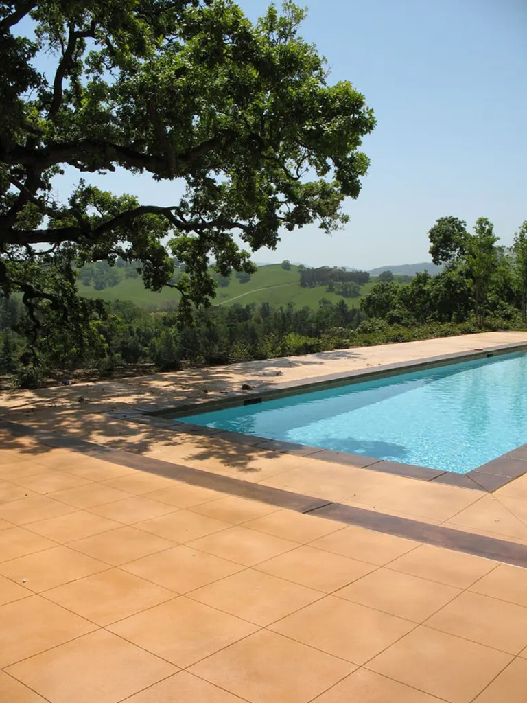 Terracotta-colored coated deck around a rectangular pool overlooking trees