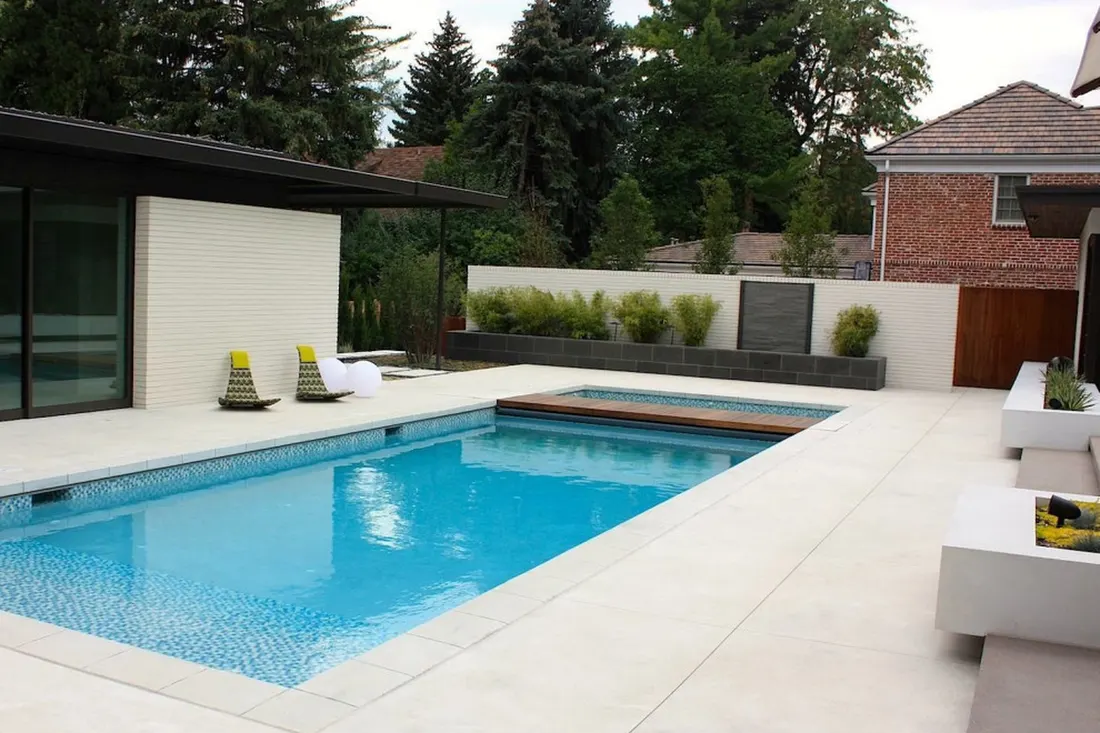 Light coated pool deck around a modern rectangular pool and lounge chairs