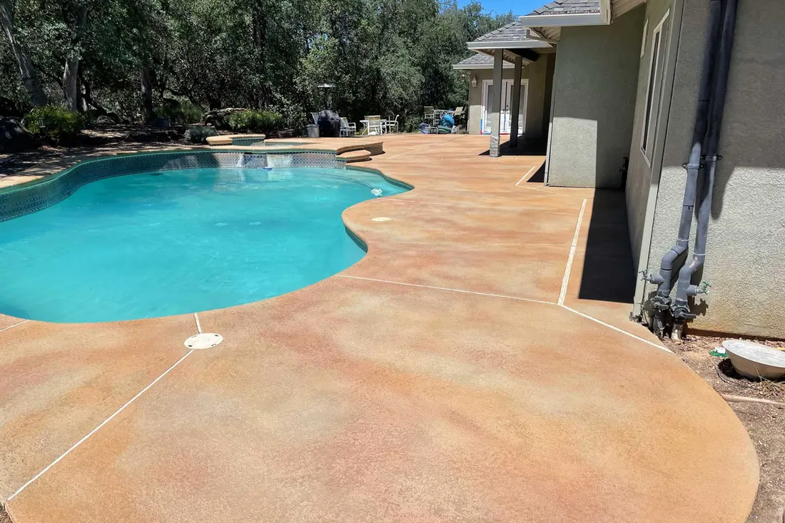 Tan and rust coated concrete deck around a curved pool beside a house