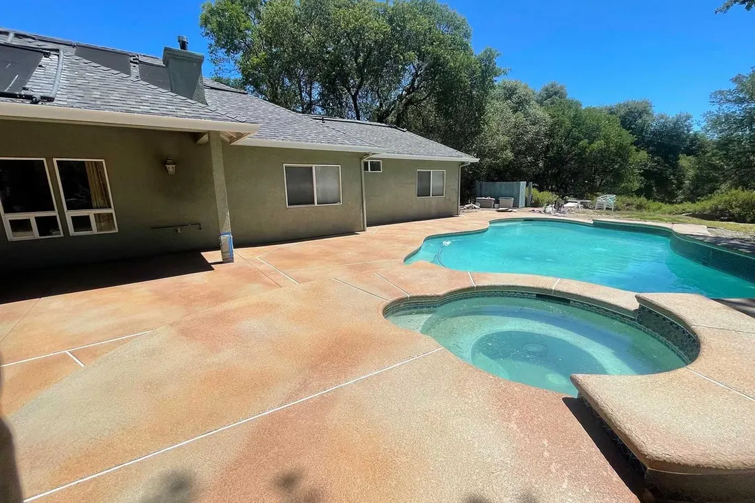 Coated pool deck around a pool and raised spa behind a ranch home