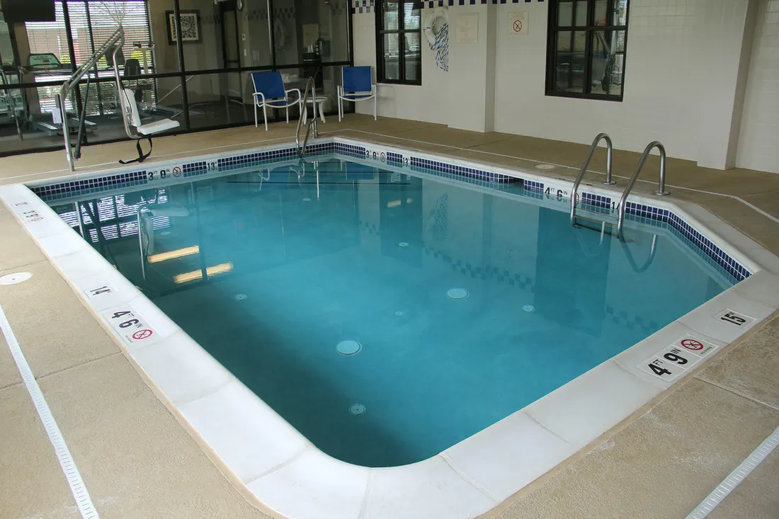 Indoor pool surrounded by a tan coated concrete deck with ladder rails