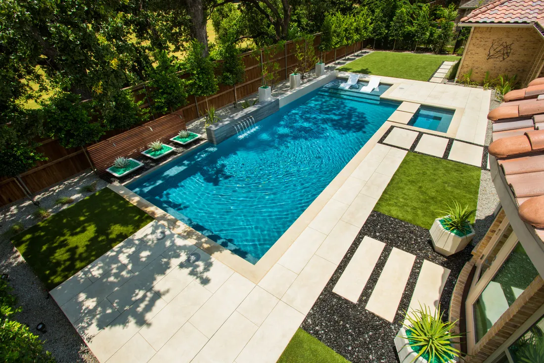 Aerial view of a rectangular pool with pale pavers and turf strips