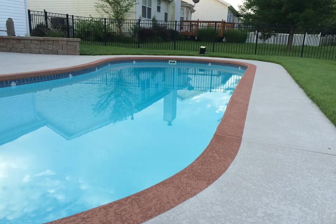 Kidney-shaped pool with a red coated border and light gray deck