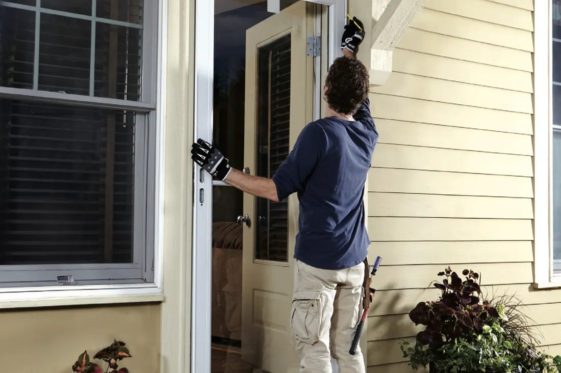 Installer fitting a white storm door on a yellow-sided house entry