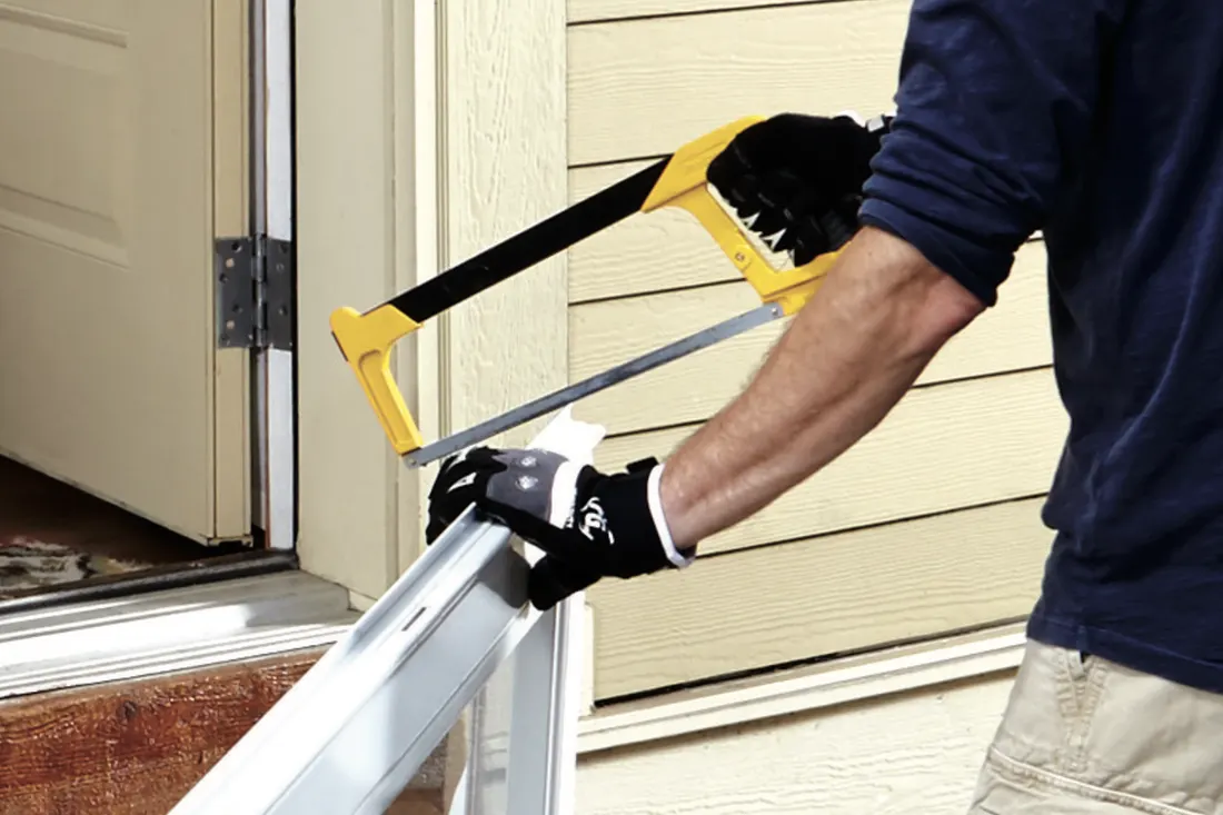 Installer cutting an aluminum storm door frame with a hacksaw