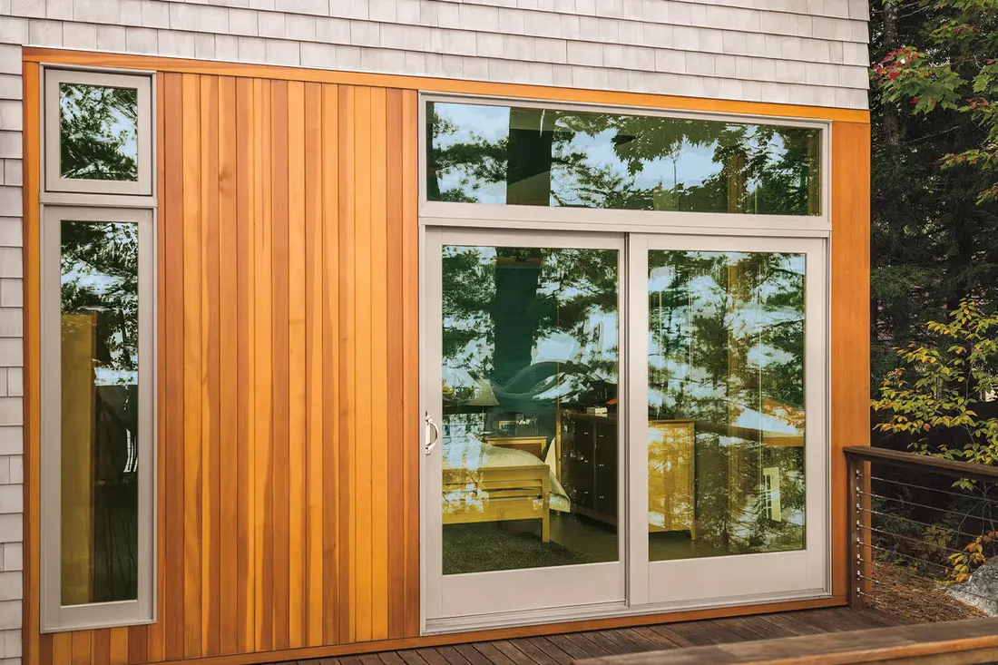 Cedar-clad wall with a white sliding patio door opening to a deck