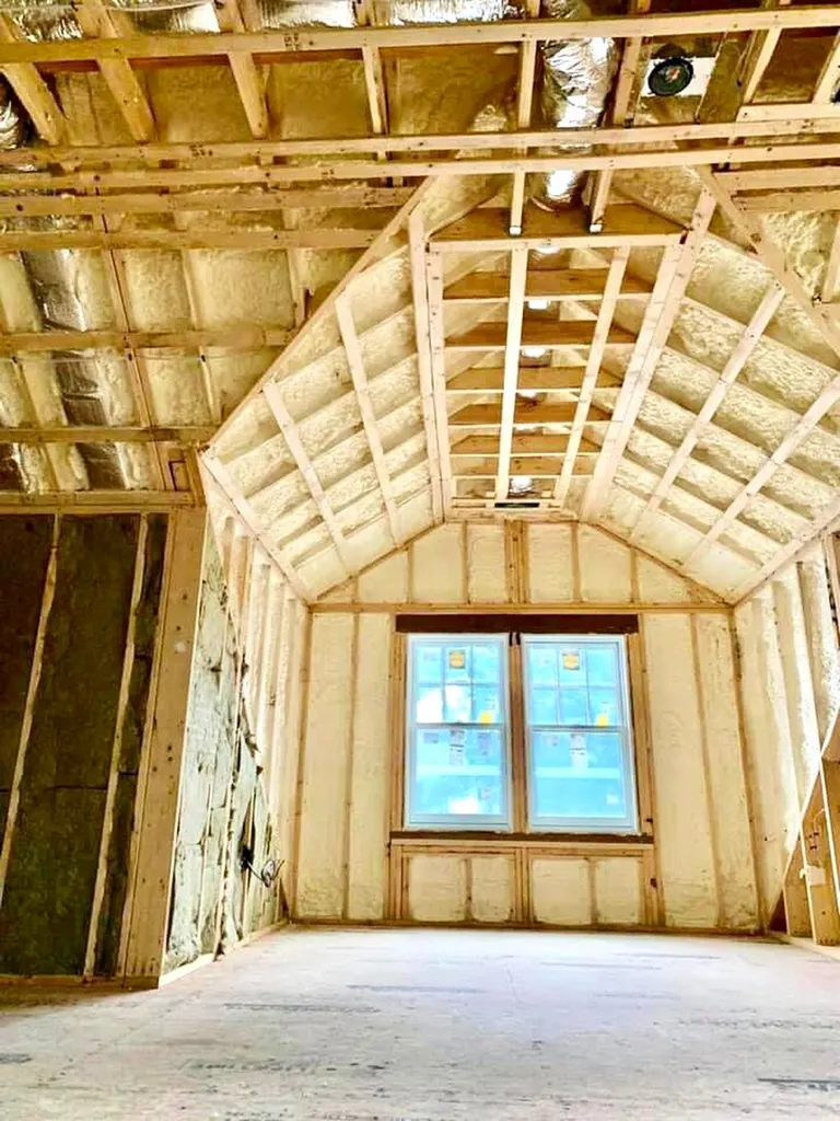 Off-white spray foam insulation applied between wood framing on walls and a vaulted ceiling