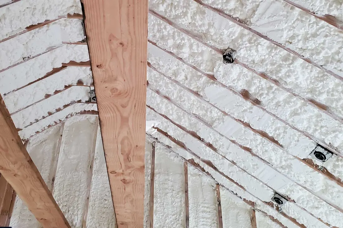 White spray foam insulation applied between wooden rafters and wall studs on a vaulted ceiling