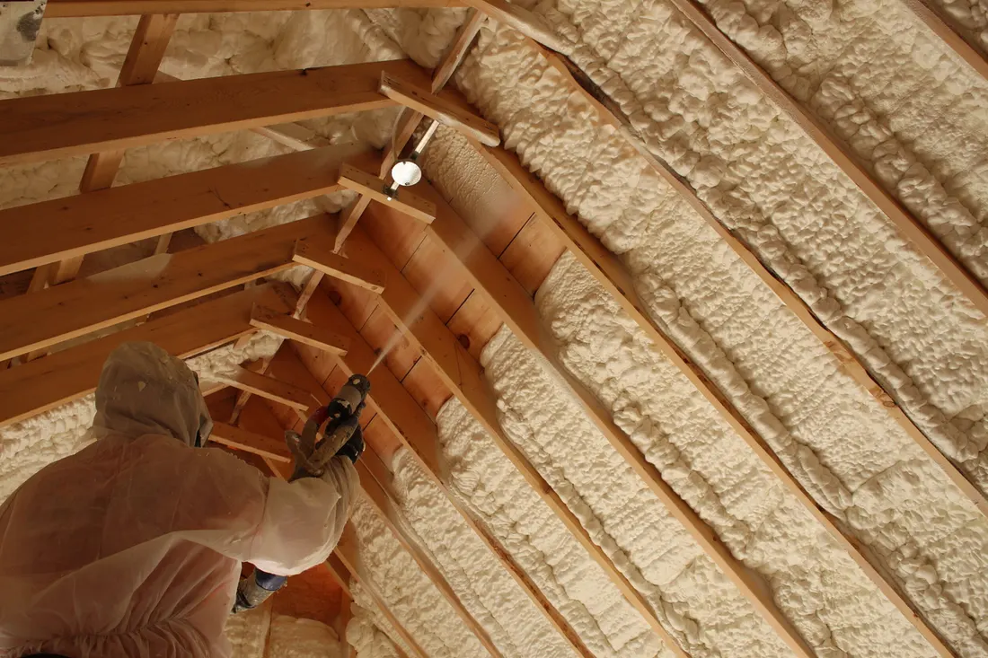 Worker in a protective suit spraying foam onto attic roof rafters