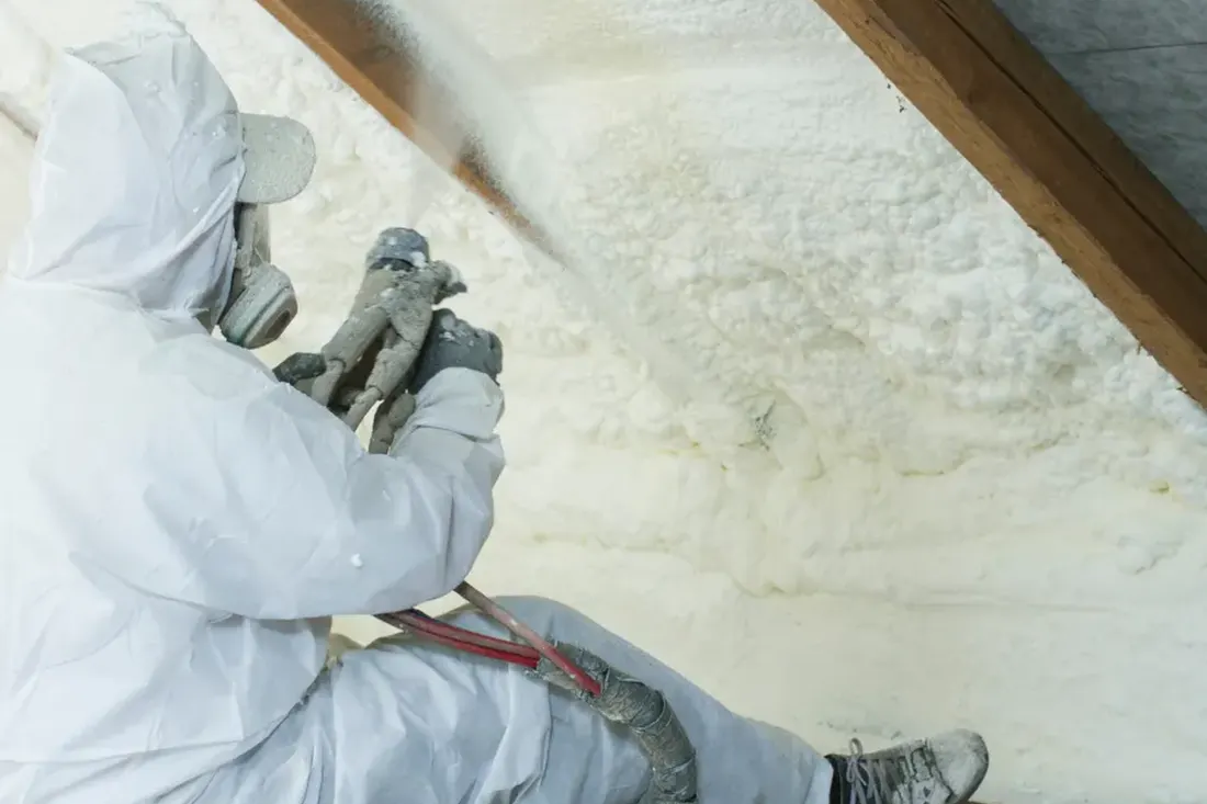Worker in protective gear spraying foam insulation on an attic slope