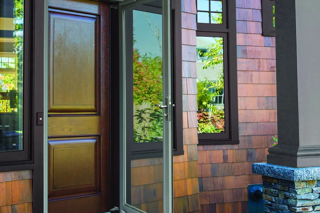 Dark wood entry door with glass storm door and shingle siding