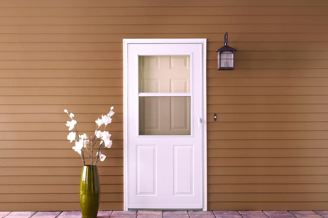 White storm door with a top glass panel on a brown sided wall
