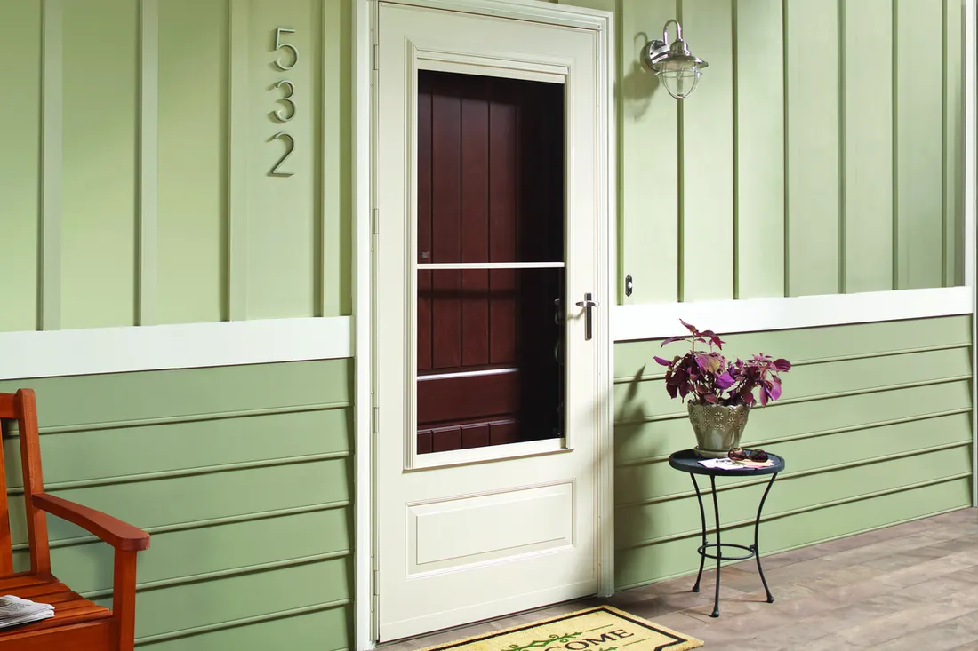 White storm door with retractable screen installed on a green-sided house porch