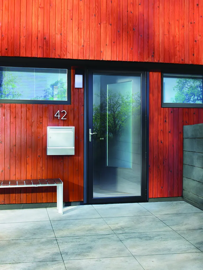 Black glass storm door on a red-clad modern entry with tile walk
